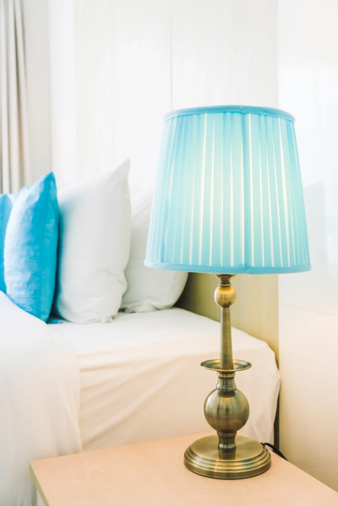 Blue table lamp with a fabric shade on a bedside table in a bright and cozy bedroom
